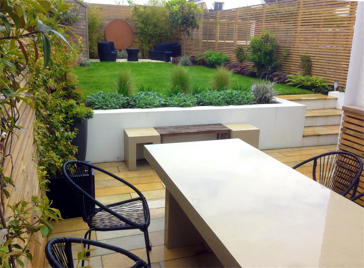 Rectilinear design for a garden in Brighton, with sawn mint sandstone paving, white rendered walls and batten screening. The garden includes evergreen tropical style planting and a corten steel circular sheet as a focal point at the rear of the garden.